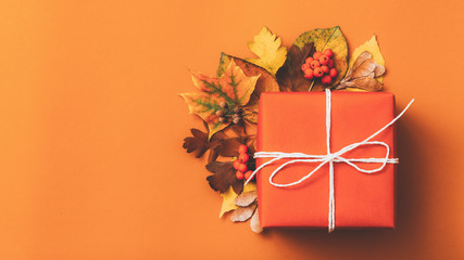 Autumn season decor. Top view of handmade paper gift box adorned with fall leaves. Orange background. Copy space.