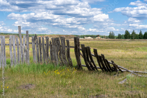 old wooden rickety fence. Abandoned field with an old wooden fence. Old broken wooden fence. Summer sunny day with blue sky and white clouds. the effects of the hurricane. Disaster