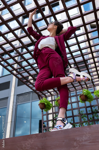 young girl showing stretching on a city street. Women's trouser suit in red. Female stretching training outdoors. Women's pants and jacket burgundy color.