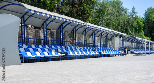 Football, stadium, area for spectators and coach. Empty blue and white plastic armchairs under a canopy. Place for text. photo