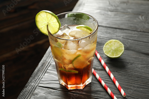 Glass of cold cola with citrus and ice on wooden table, space for text