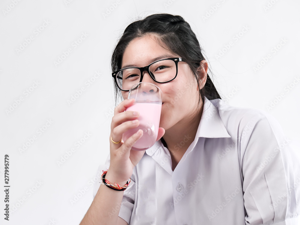 Happy Asian student in uniform drinking strawberry milk in glass on white background. Happy Asian student in uniform drinking strawberry milk in glass on white background.
