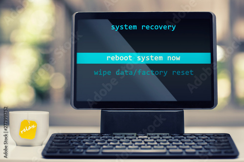 A tablet device with system recovery on the screen and about to be rebooted in a modern work setting with a tea cup that says relax.
