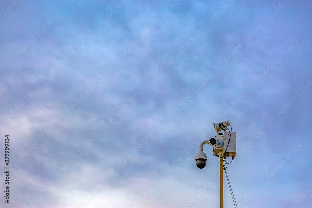 Outdoor security camera isolated against a cloudy blue sky background Outdoor security camera isolated against a cloudy blue sky background