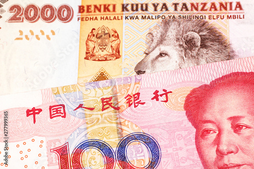 An orange and white two thousand Tanzanian shilling note with a red Chinese, one hundred yuan renminbi note in macro photo