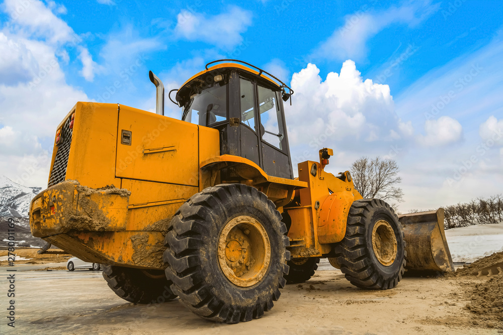 Close up of a dirty yellow loader with black rubber wheels and empty cab