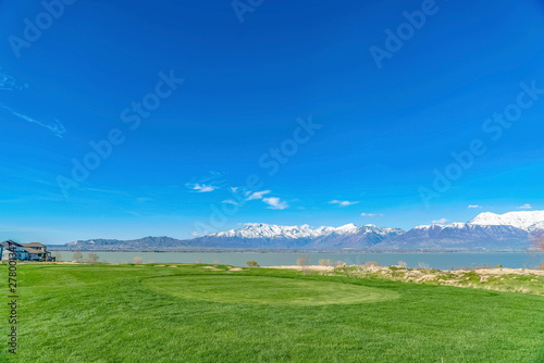 Lush grassy terrain with view of a calm lake and towering snow topped mountain © Jason