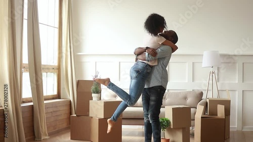 Happy african husband carrying spinning wife celebrate moving day
