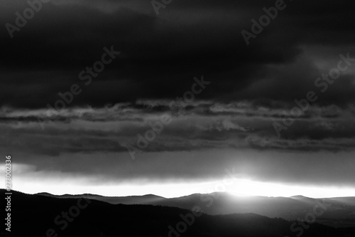 View of dark clouds at sunset, with sun filtering through an hole over the mountain