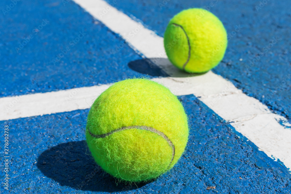 Two tennis balls on a blue tennis court with white marking lines