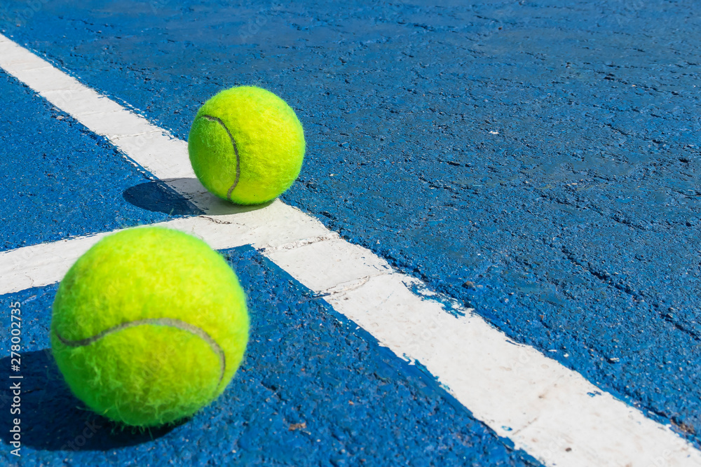Two tennis balls on a blue tennis court with white marking lines