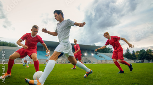 Professional Soccer Player Leads with a Ball, Masterfully Dribbling and Bypassing Sliding Tackles of His Opponents. Two Professional Football Teams Playing. Low Angle Shot. photo