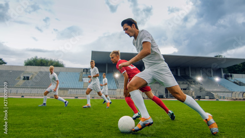 Professional Soccer Player Leads with a Ball, Masterfully Dribbling and Bypassing Sliding Tackles of His Opponents. Two Professional Football Teams Playing. Low Angle Shot. © Gorodenkoff