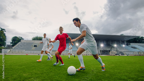 Professional Soccer Player Leads with a Ball, Masterfully Dribbling and Bypassing Sliding Tackles of His Opponents. Two Professional Football Teams Playing. Low Angle Shot. © Gorodenkoff