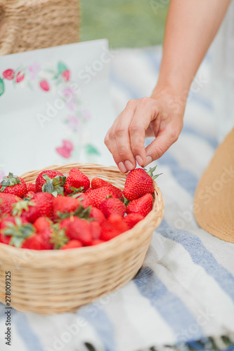 Close-up. Young beautiful pregnant woman in white dress is sitting in the meadow and eating strawberries. Picnic. Motherhood.