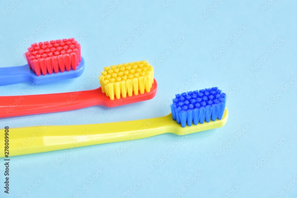 Three colorful plastic toothbrush with selective focus on blurred blue background. Multicolored toothbrushes for personal daily healthcare. Toothbrushes for daily oral hygiene and caries protection Three colorful plastic toothbrush with selective focus on blurred blue background. Multicolored toothbrushes for personal daily healthcare. Toothbrushes for daily oral hygiene and caries protection