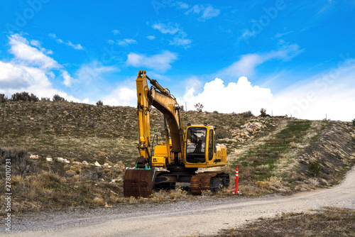 Yellow excavator and orange traffic delineator post beside a mountain road