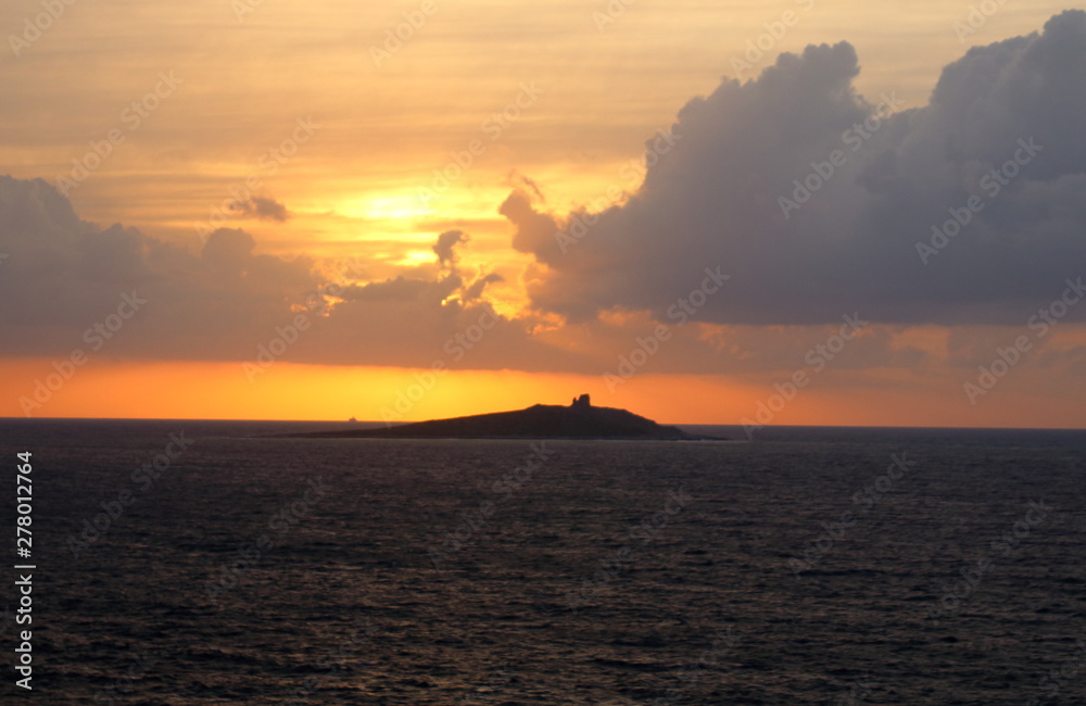 evocative image of sunset over the sea with island in the background and clouds evocative image of sunset over the sea with island in the background and clouds