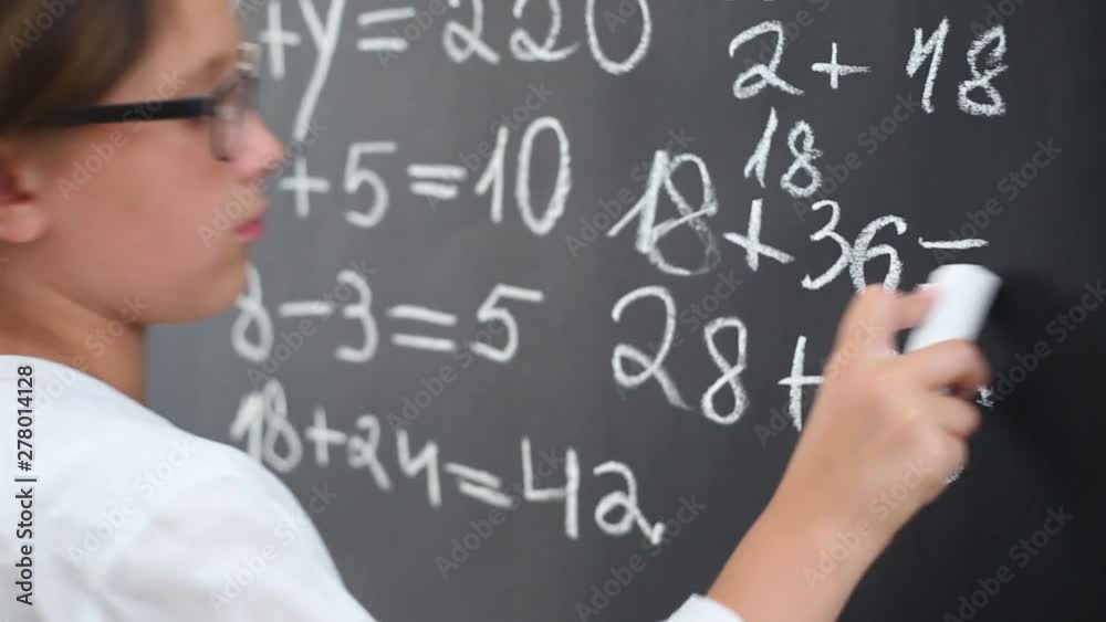 The girl in glasses writes with chalk on the school board in class. The girl in glasses writes with chalk on the school board in class.