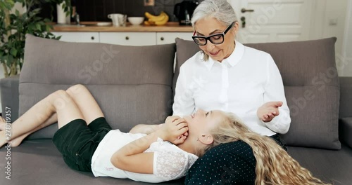 Grandmother stroking preteen girl's hair, granddaughter lying on senior ladies hands and feeling relaxed