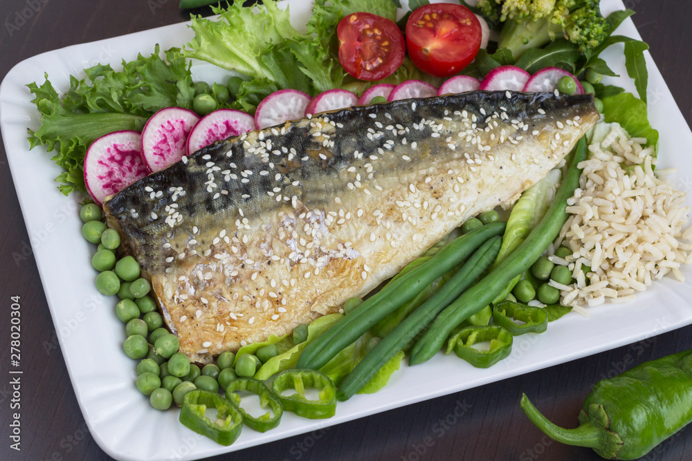 Grilled fish sprinkled with sesame with vegetables, rice. Black background Grilled fish sprinkled with sesame with vegetables, rice. Black background