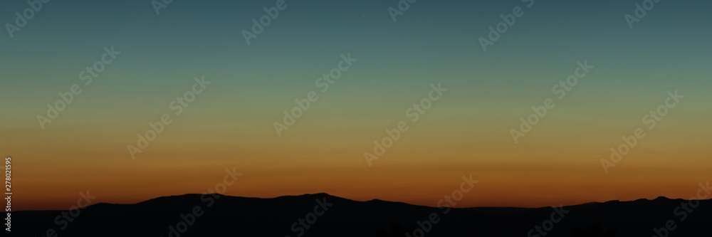 Wide angle panorama silhouette mountain tops in orange blue gradient sunset