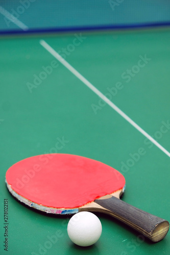 Table tennis racket with a ball on green background.