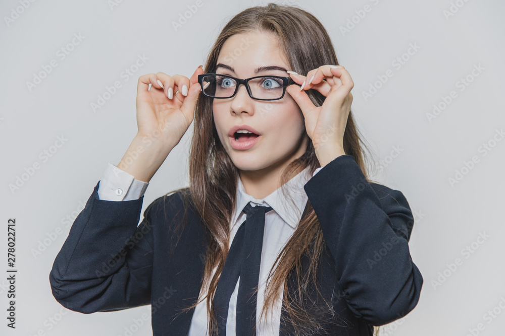 Close up portrait of a dazzling and astounded businesswoman, who is touching the black rim of glasses with both hands and opens her mouth slightly.