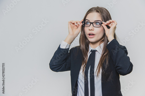 Close up portrait of a dazzling and astounded businesswoman, who is touching the black rim of glasses with both hands and opens her mouth slightly.
