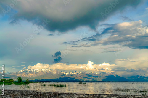 Picturesque view of shiny lake and snow topped mountain under cloudy sky