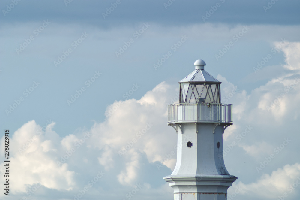 The top of a white lighthouse against a white cloud backdrop 