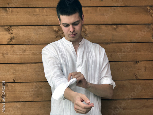 Young attractive man rolling up sleeves of white shirt close-up across wooden wall. Copy space