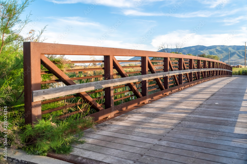 Bridge over a lake with view of mountain and valley under blue sky and clouds