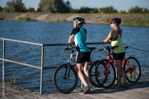 Two friens female with bikes standing on the pierce and looking at the water