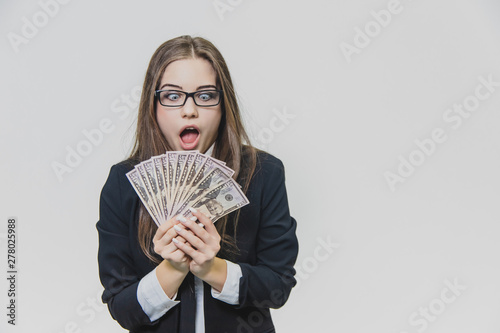 Shocked, excited young business woman is showing a pile of money, isolated on white background. Girl has a lot of money. Cheerful girl is opening her mouth, because of astonishment of having money