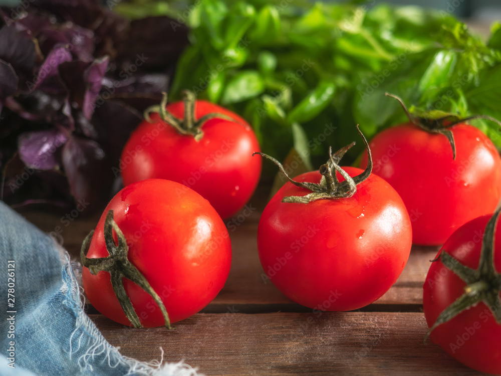 Ripe red tomatoes and fresh lettuce of different varieties lie on the Board table Ripe red tomatoes and fresh lettuce of different varieties lie on the Board table