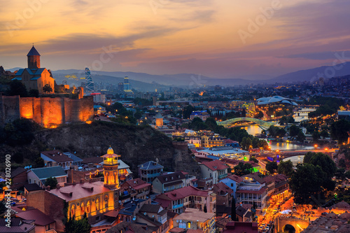 Beautiful view of the Georgian capital Tbilisi at sunset Narikala fortress in the foreground, Kura river with a bridge and mountains in the background.
