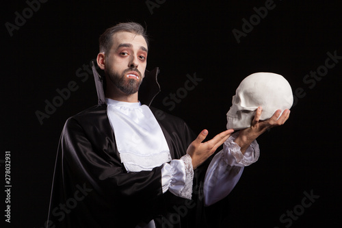 Attractive man in Dracula costume and vampire theet holding a human skull photo
