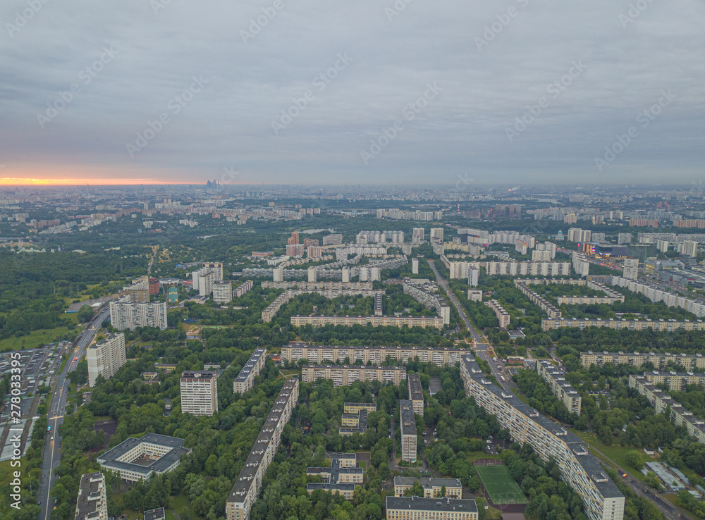 Aerial view of the city district with tall residential buildings, roads and highways, park zones and yards with green trees. Summer urban landscape under сlear sky at sunrise. Moscow city, Russia