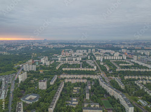 Aerial view of the city district with tall residential buildings, roads and highways, park zones and yards with green trees. Summer urban landscape under сlear sky at sunrise. Moscow city, Russia