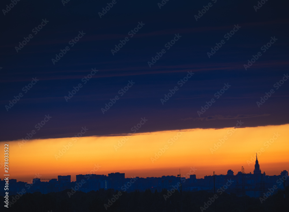 Dark cloudscape on sunset with stripe of the clear sky, over the panoramic silhouette of the buildings. Moscow city skyline, evening urban landscape.