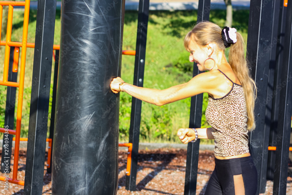 Obraz premium Woman boxer boxing a punching bag outdoors, doing workout. Athletic girl in sportswear training, standing in boxing position with fists