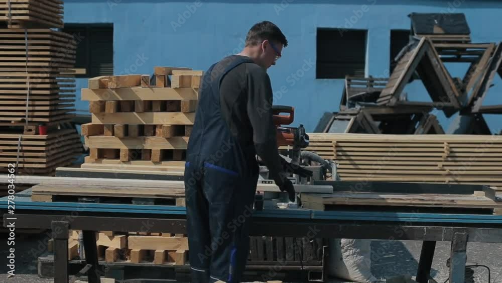 Rear view of Industrial young carpenter worker in special uniform using wood cutting machine. Rear view of Industrial young carpenter worker in special uniform using wood cutting machine.