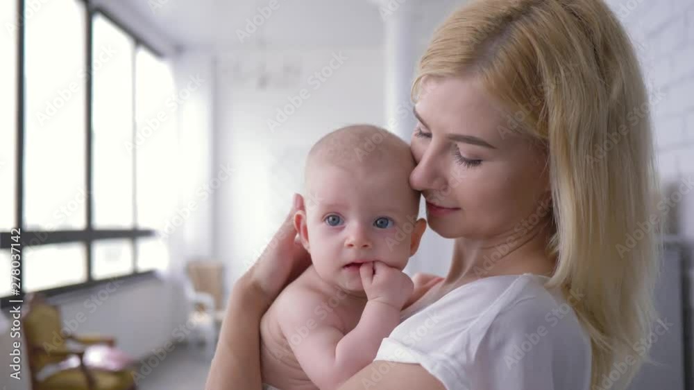 portrait of mom and newborn baby, happy young woman holding on hands a little girl and gently kissing her portrait of mom and newborn baby, happy young woman holding on hands a little girl and gently kissing her