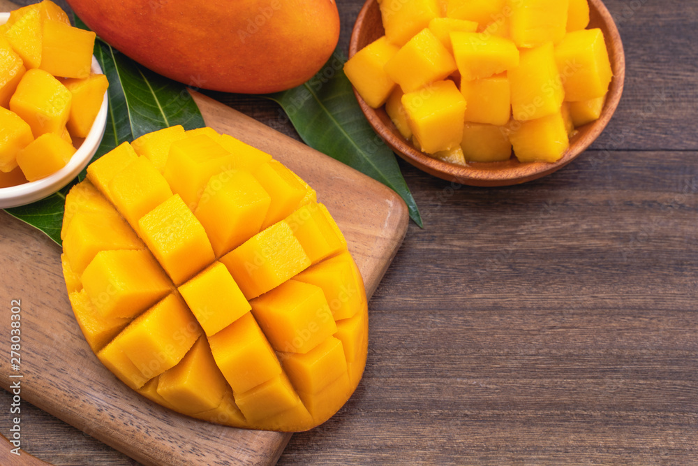 Fresh Mango - Juicy chopped mango cubes on wooden cutting board and rustic timber background. Tropical summer concept. Close up, macro, copy space.