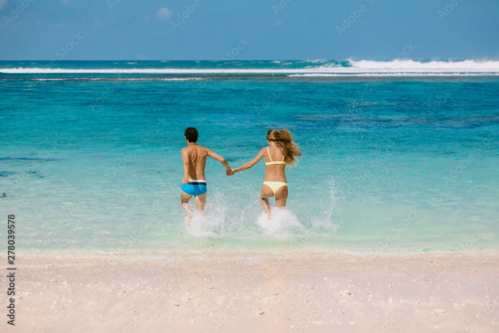 Happy running couple. Pregnant woman with husband expecting baby at tropical beach with blue ocean Happy running couple. Pregnant woman with husband expecting baby at tropical beach with blue ocean