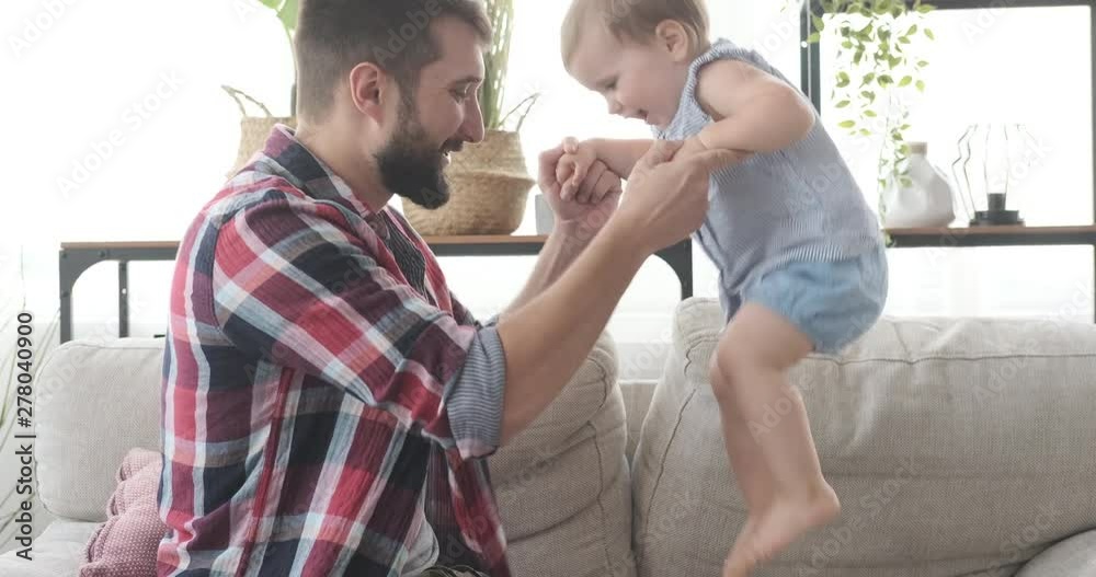 Father with cute baby daughter jumping on sofa at home Father with cute baby daughter jumping on sofa at home