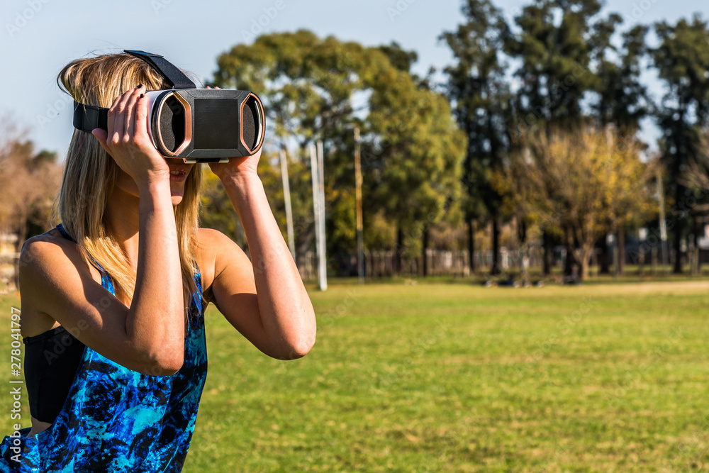 Caucasian woman in the park, blonde with virtual reality mask on a sunny day with blue sky