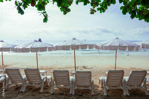 Landscape view of sea beach in the morning, Beach umbellas and bench on seaside with green tree, Summer adventure in Samed Island in Thailand, Vibrant sea with clouds on horizon in morning photo