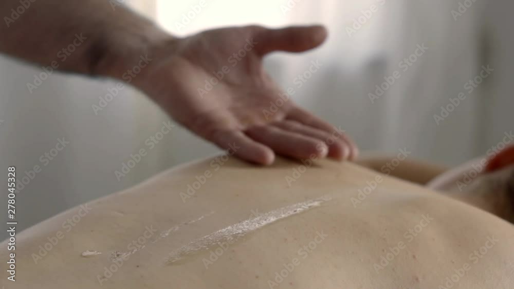 massagist is applying lotion on back of patient lying in room on table massagist is applying lotion on back of patient lying in room on table